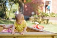 Young kid playing in sandbox outside house.