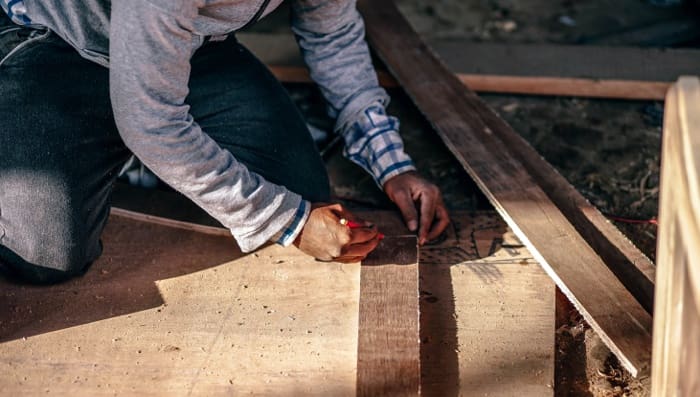 Man kneeling on the ground measuring plywood to cut.