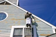 Man on ladder painting exterior of house with chipped paint.