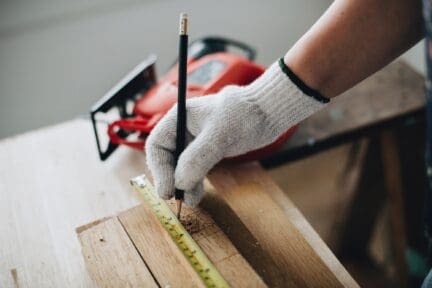 Home maintenance professional measuring wood to be cut with red saw.