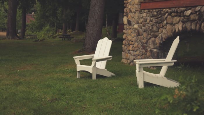 two white adirondack chairs on green sloped lawn.