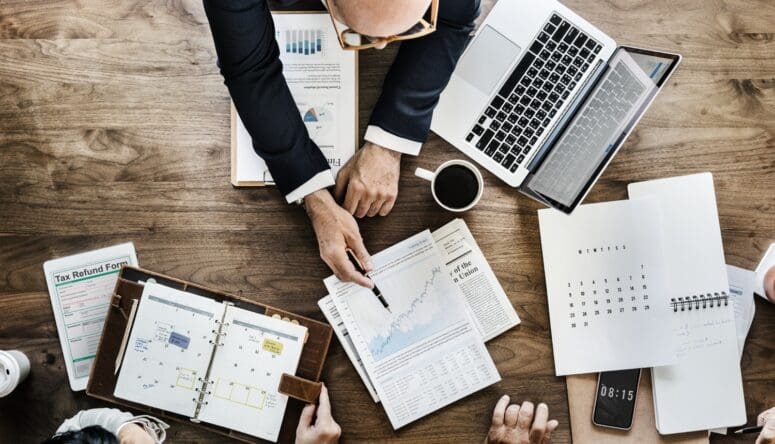 Male real estate agent in business meeting pointing to real estate projections on a graph.