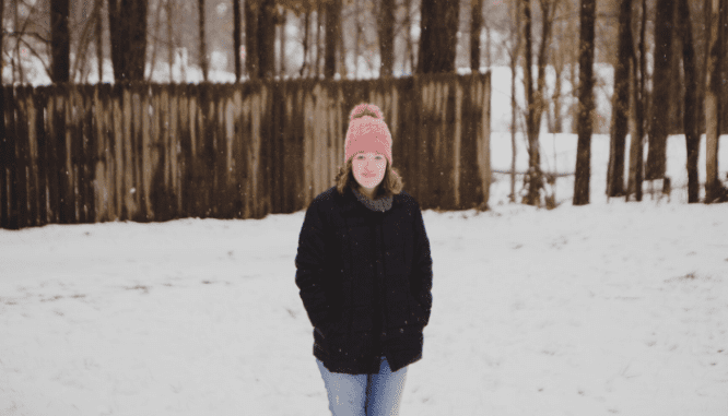 A woman standing in front of her home while it snowing.