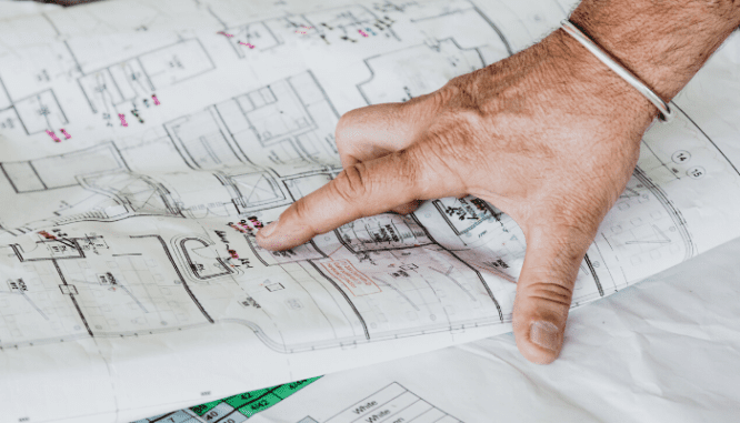 A man's hand pointing at renovation blueprints.