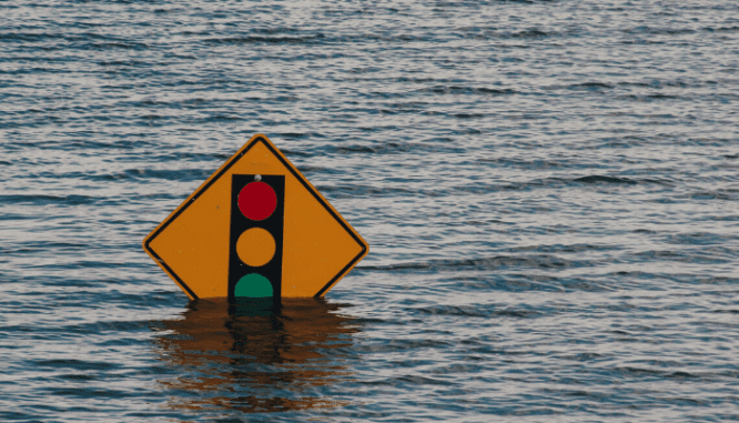 A traffic sign showing a stoplight is partially underwater.