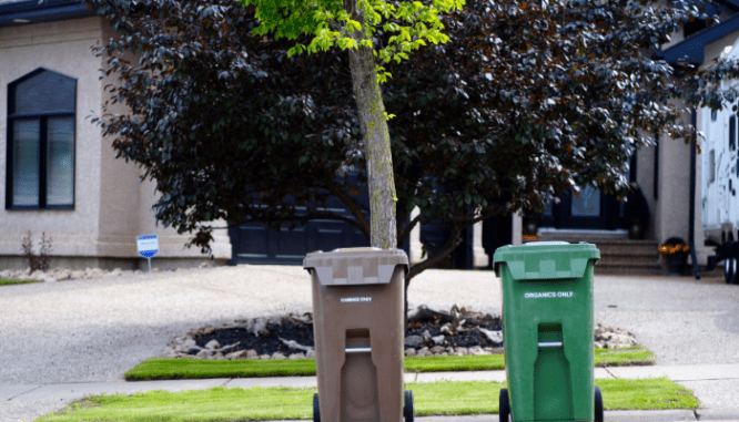 Two trash cans in front of a house that are outdoor eyesores.