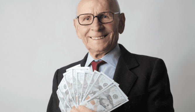 An older banker holding fanned out $100 bills for a house.