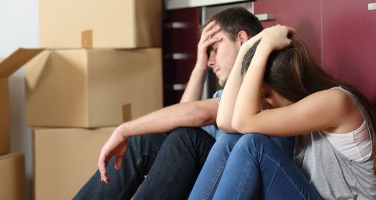 A stressed-out couple surrounded by moving boxes who are buying a house during coronavirus