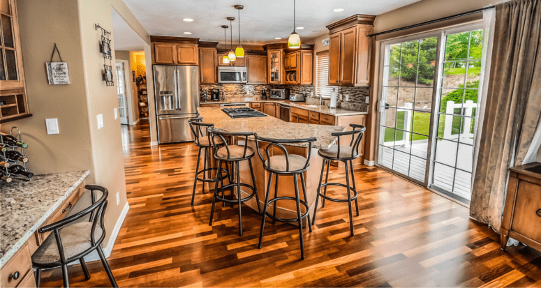 Bar chairs around a kitchen island in a kitchen with wood floors and cabinets.