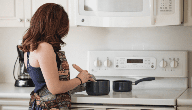 A woman wearing a printed apron cooking in a white kitchen. in order to save for a house in 3 years.