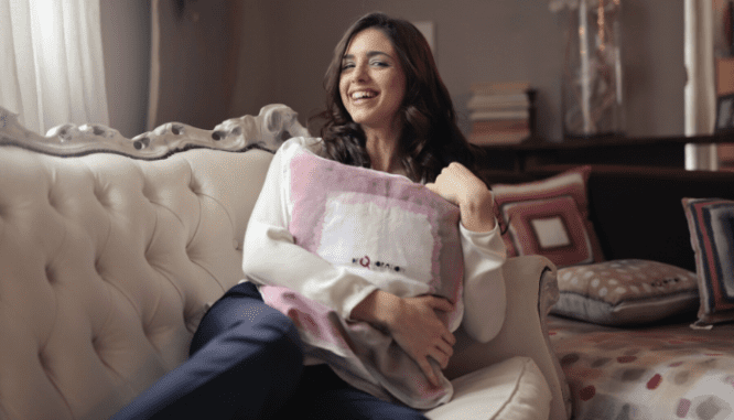 A smiling woman hugging a pillow to herself on a white antique sofa in a house you could rent or buy.