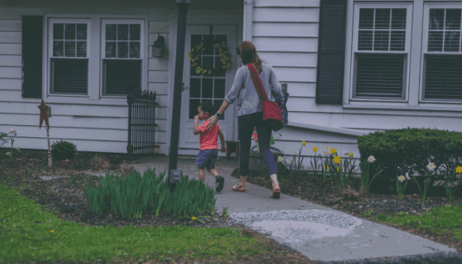 A woman walking with a young boy toward the front door of a white house they could rent or buy.