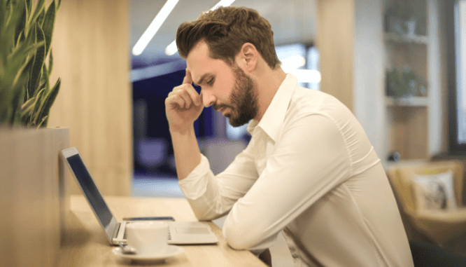 A man with his hand on his head, looking frustrated while looking down at a laptop.