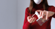 A person in a red long-sleeved shirt and mask holding a small bottle of hand sanitizer to use for moving during coronavirus.