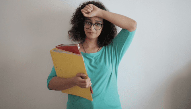 A woman with curly hair wearing a green shirt and glasses, and holding colored binders looking frustrated because a buyer rejected her counter offer..