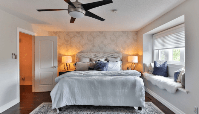 A gray and blue themed bedroom with a ceiling fan and reading window nook.