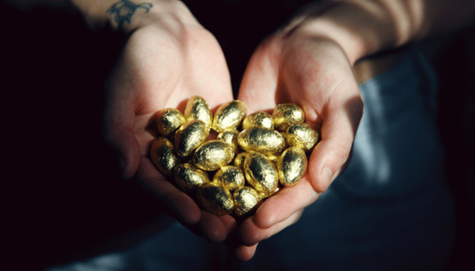 Hands holding out handfuls of little gold foil eggs.