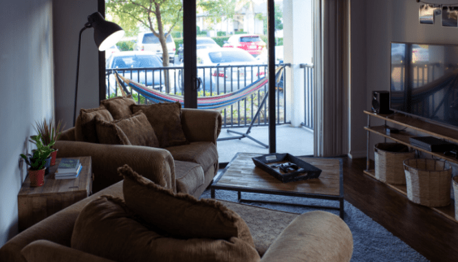 The view of a hammock on a balcony through a tan and brown themed living room.