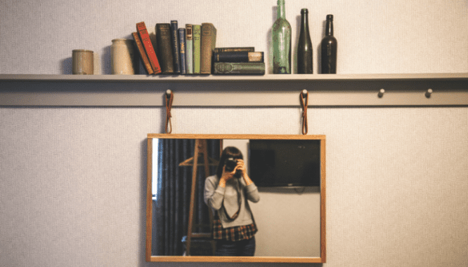 A woman taking a photograph while moving a bookshelf, and you can see her in the mirror.