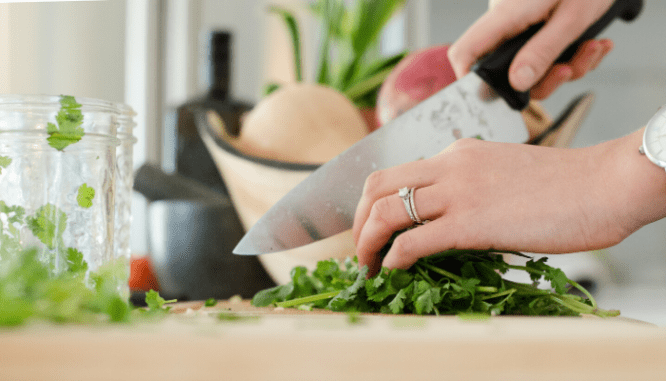 A hand with a diamond wedding ring chipping herbs on a cutting board.