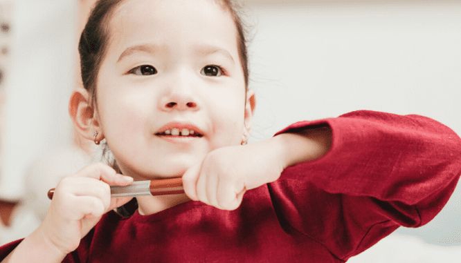 A small girl of Asian descent wearing a red shirt is taking off a marker cap in order to help label for moving in a hurry.