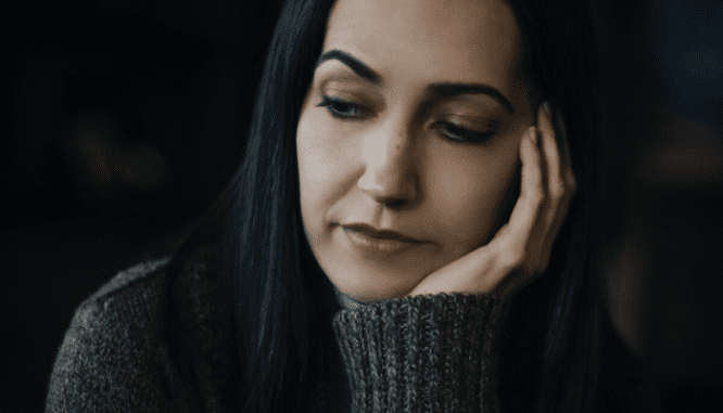 A woman in a dark sweater with dark hair looking sad with buyer's remorse.