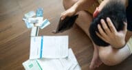 A house poor man sitting on the floor surrounded by credit cards and bills.