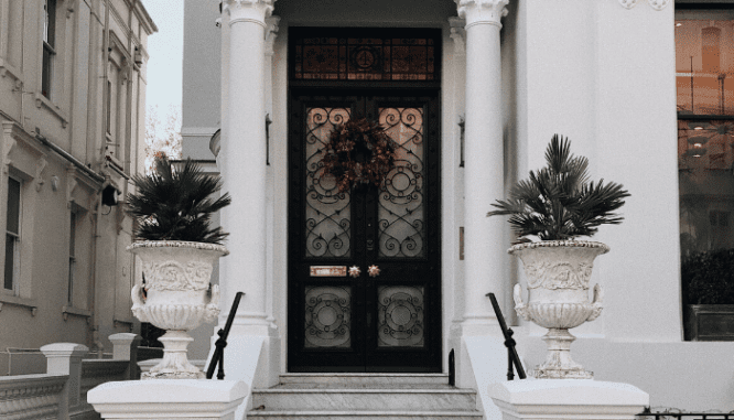 A dark brown front door with grand potted plants and a wreath between two columns.