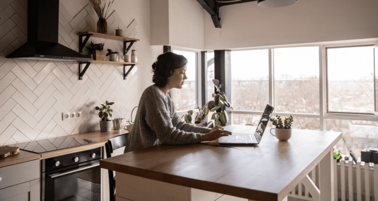 A woman sitting at a kitchen counter using a computer to learn how to build credit without a credit card.