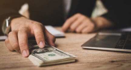 A man pushing a stack of cash across a table signifies an all cash offer