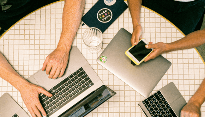 A group of people using laptops and a cell phone in order to buy a house online.