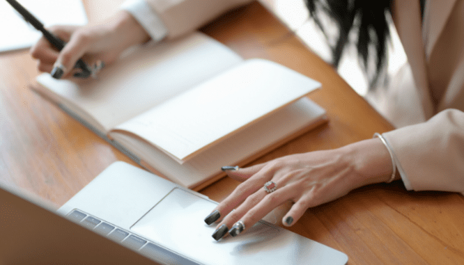 A woman's hands with professional nails and a ruby ring doing paperwork in front of a laptop to find out if rent to own homes build credit.