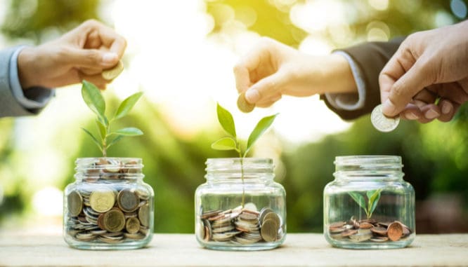 Three hands dropping coins into three different jars to show how crowdfunding is one way to invest 5000 dollars in real estate