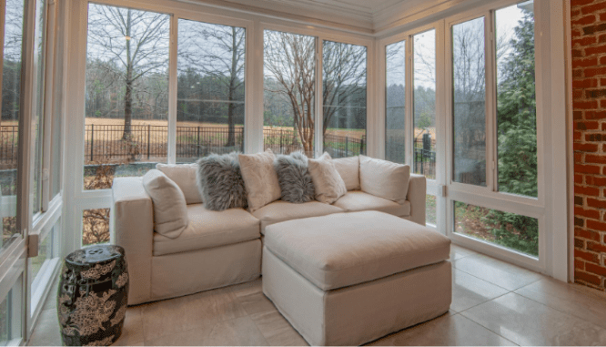 A white sofa with furry throw pillows in a windowed room with an ottoman, an example of optimizing the furniture arrangement in a new house.