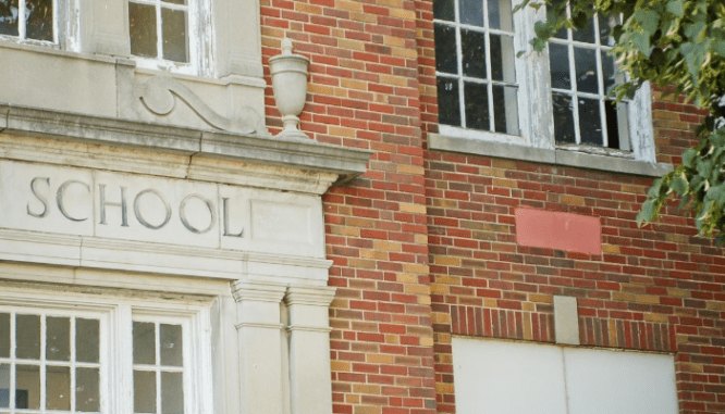 A closeup of a red brick school building with white trimmed windows which could have an impact on property values.