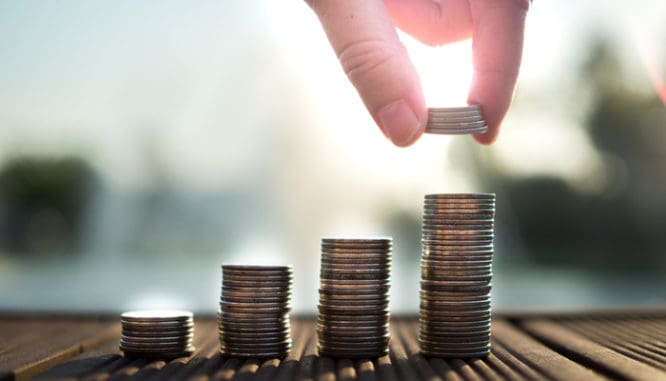 A hand putting money into a growing stack symbolizing how you increase your homeowner liability insurance