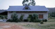 A gray brick house with pine shrubbery and wooded windows that could need repairs after a home inspection.