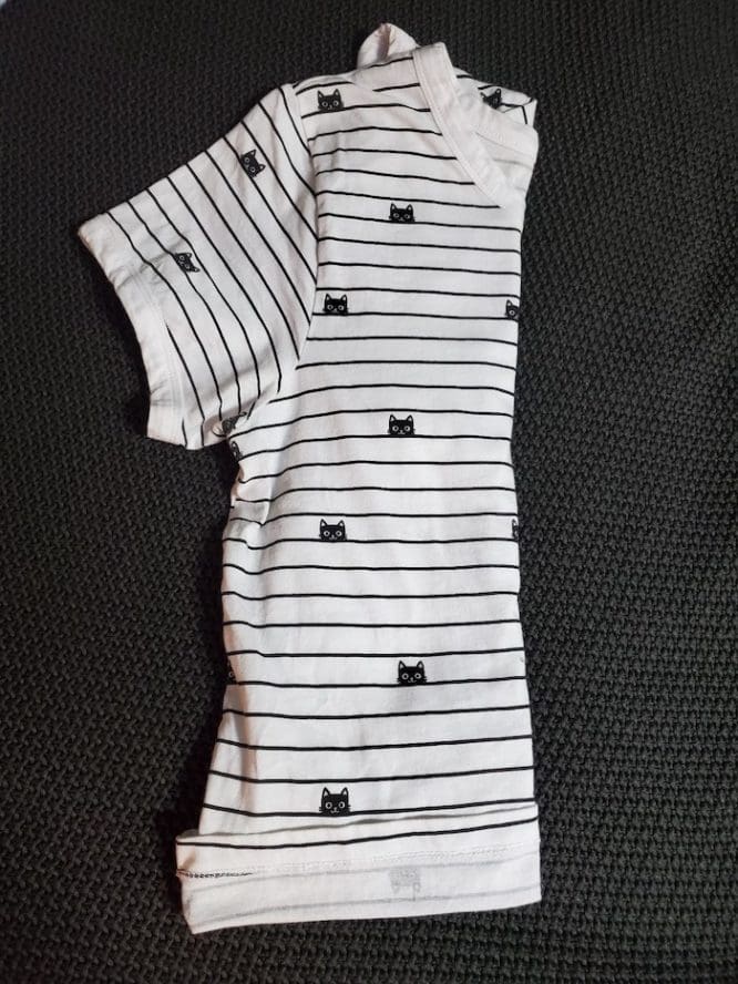 A shirt with a lined cat print with its last side folded in half in a military roll to show how to pack clothes for moving