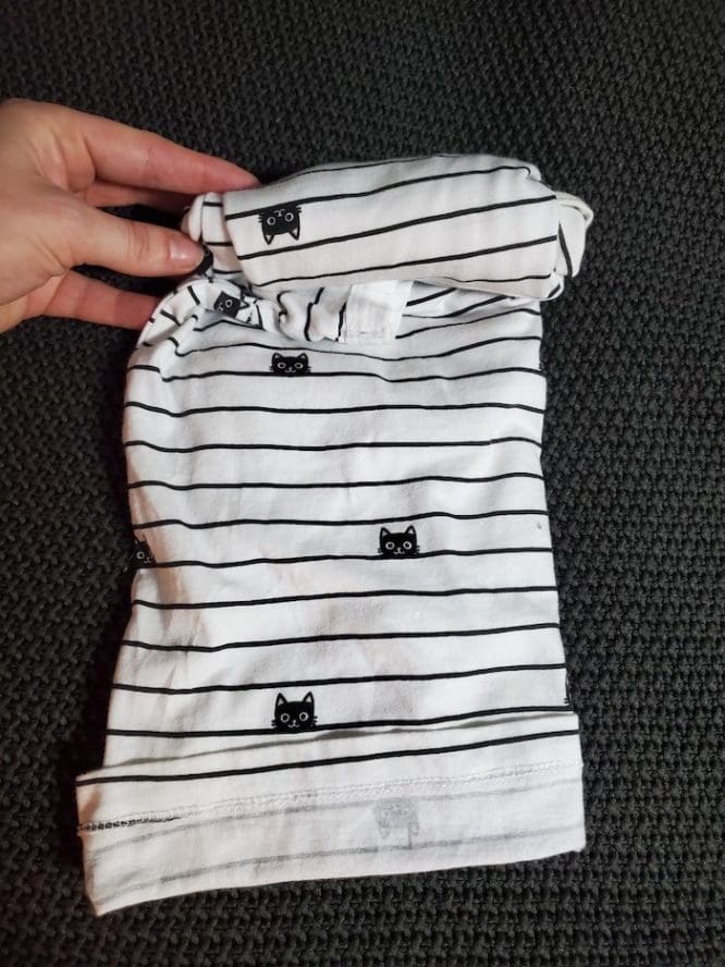 A shirt with a lined cat print getting rolled up into a military roll pouch to show how to pack clothes for moving