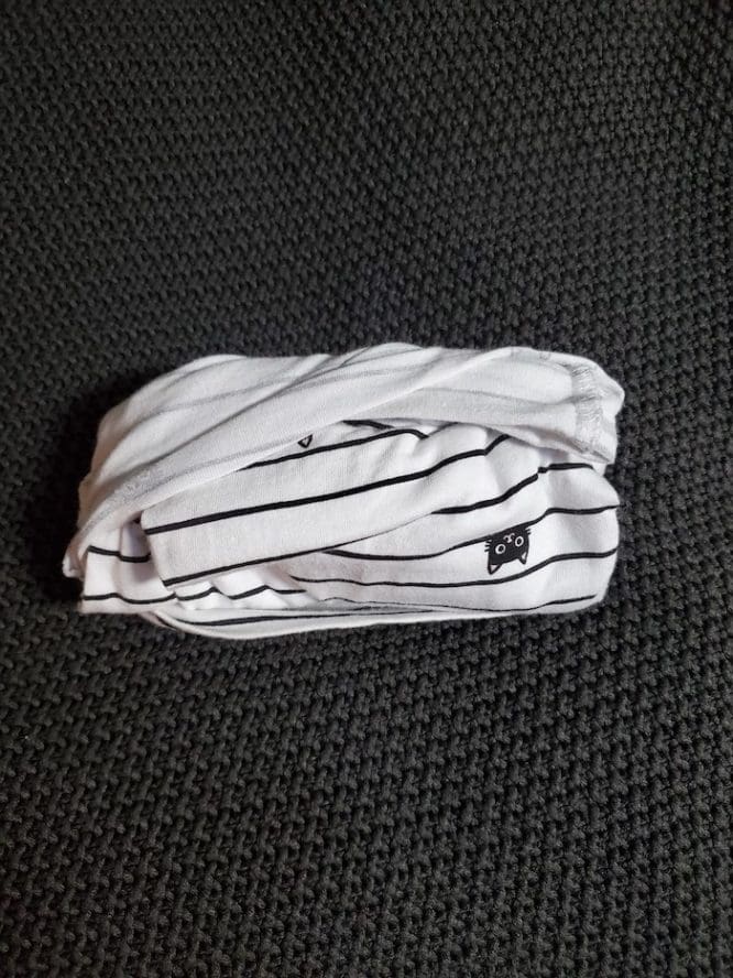 A shirt with a lined cat print rolled up in a military roll to show how to pack clothes for moving