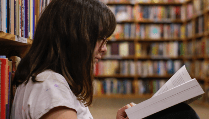 A woman with glasses and brown hair at a library reading a book on how foreclosure auctions work.