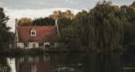 A brick home along the riverside with willow trees around it.