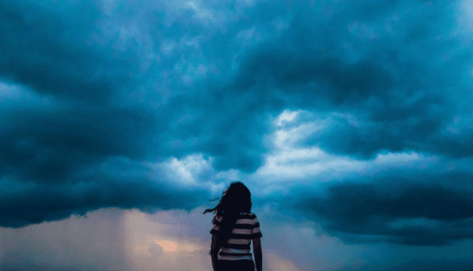 A person looking at a storm near a waterfront home.