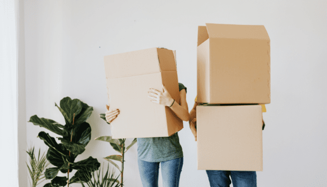 A couple holding moving boxes after selling real estate.