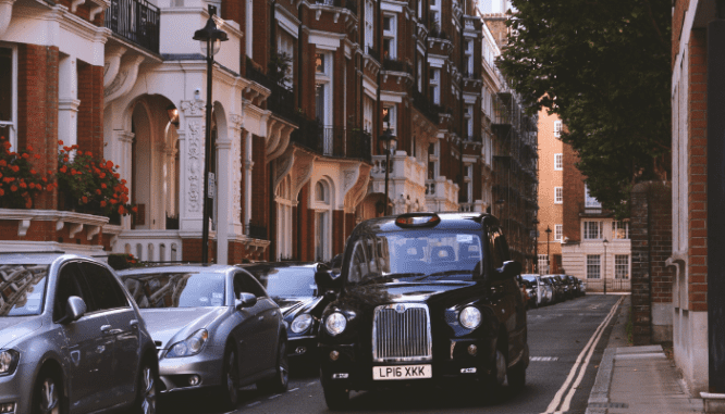 An image of a car in front of a brownstone used to depict what a brownstone is.