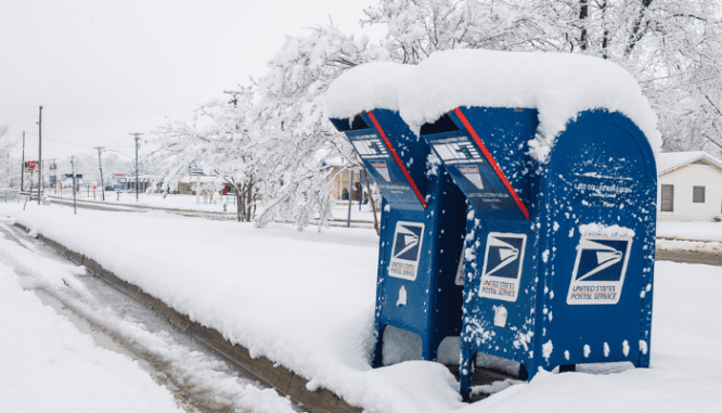 Blue post office deposit boxes on a street of snow.