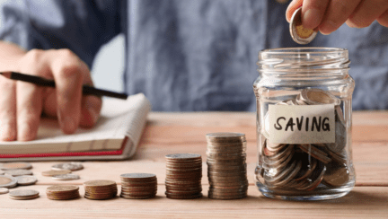 A man puts coins in a jar to symbolize investments to save for a house.