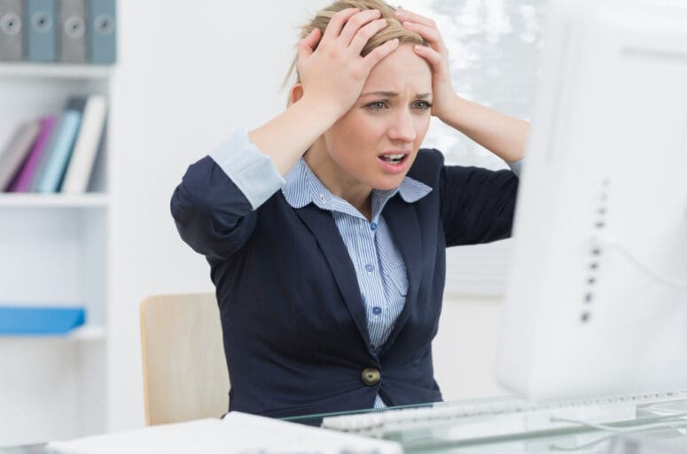 Frustrated business woman sitting with head in hands in front of computer at office desk