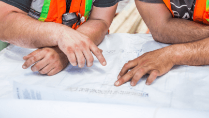 Construction workers with blueprints for building a house in Michigan, wondering about the average cost.