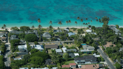 An aerial view of houses by a beach shore in Hawaii where houses sell for cash